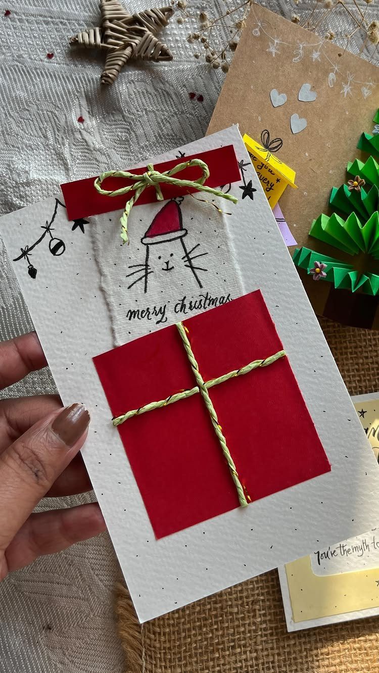 Handmade white Christmas card with a red gift illustration and a cute cat drawing.