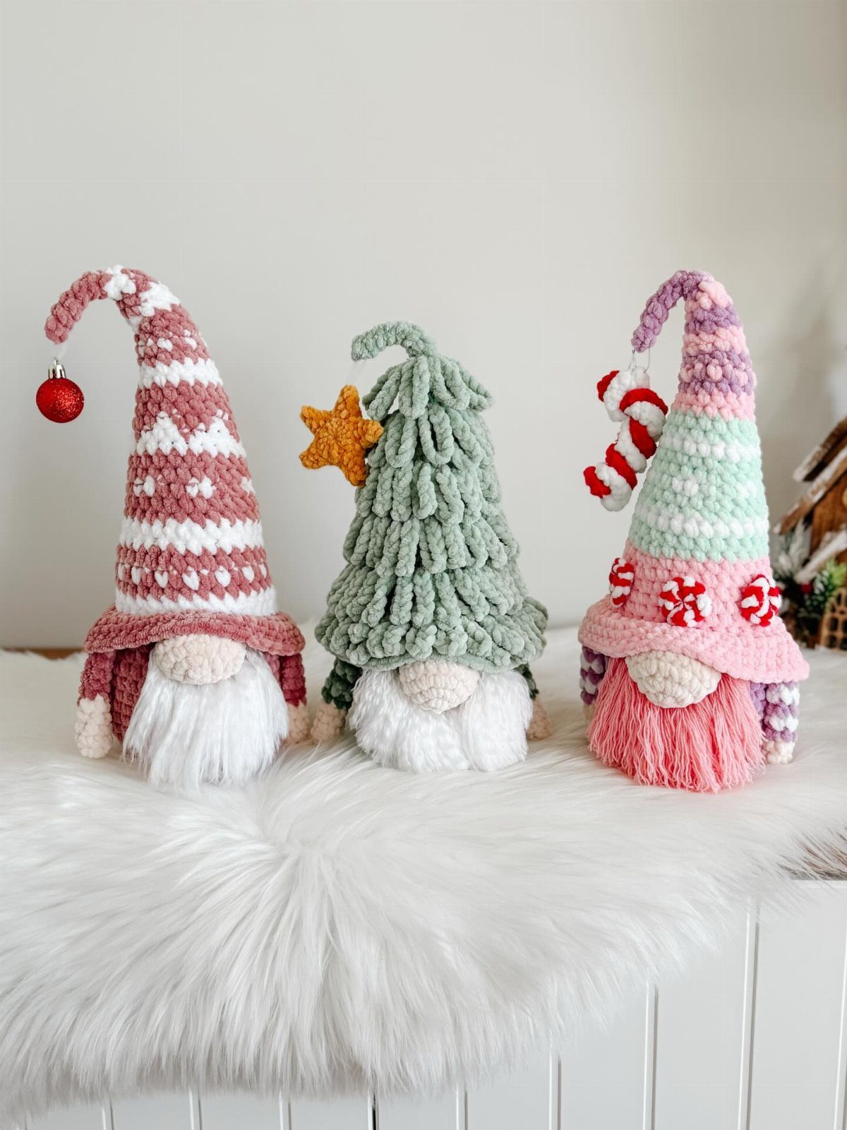 Three colorful crocheted Christmas gnomes with long hats and beards on white fur.