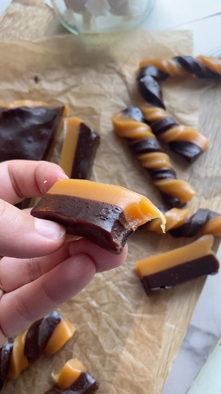 Two-toned chocolate and caramel candies on parchment paper, one held by a hand.