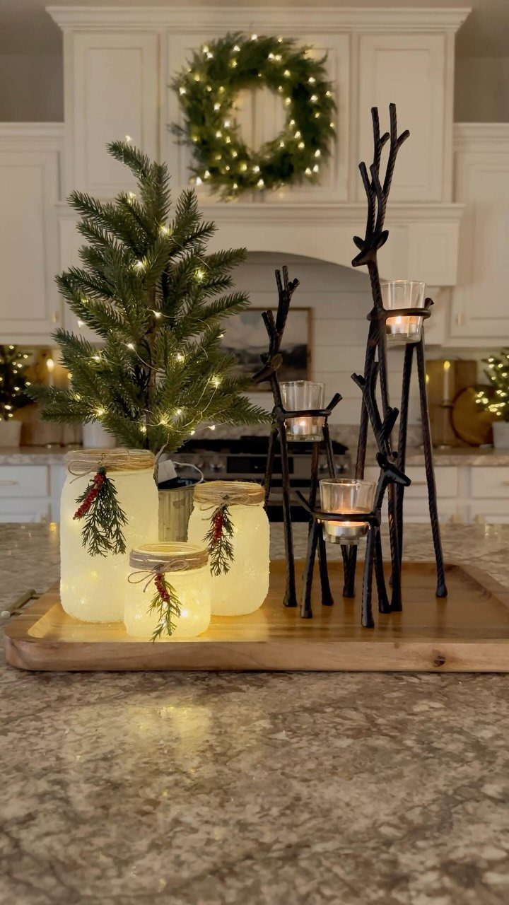 Frosted mason jar luminaries with tea lights and greenery on a wooden tray.