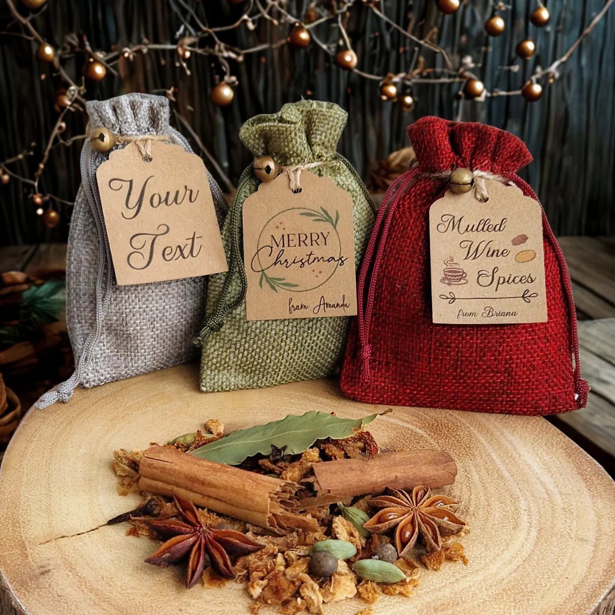Three colorful fabric spice sachets with tags and loose mulling spices on wood.