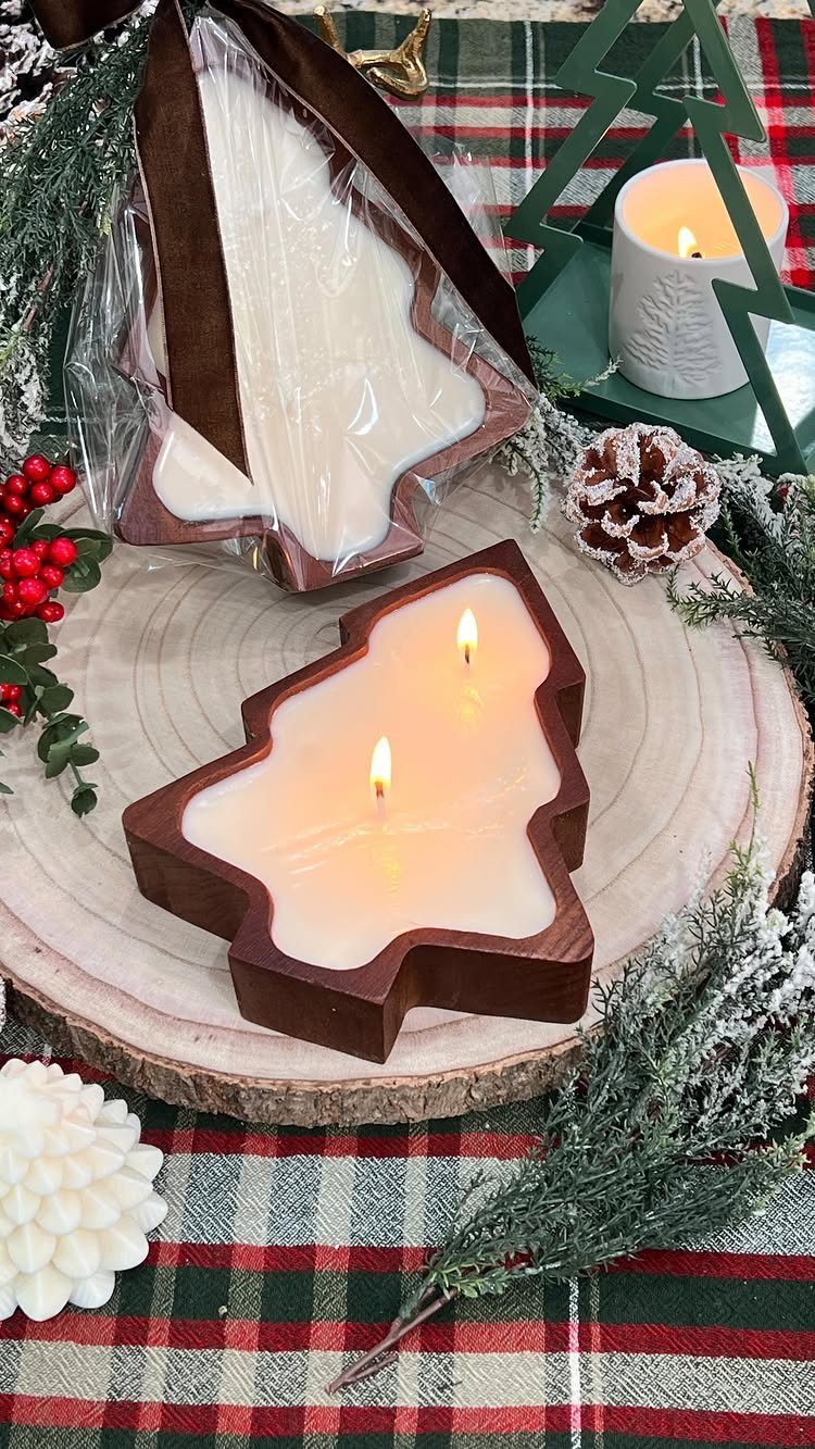 Tree-shaped candles in wooden holders on a rustic wooden slice with holiday greenery.