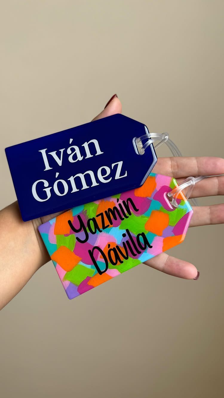 Two personalized luggage tags, one blue and one multicolored, held in a hand.