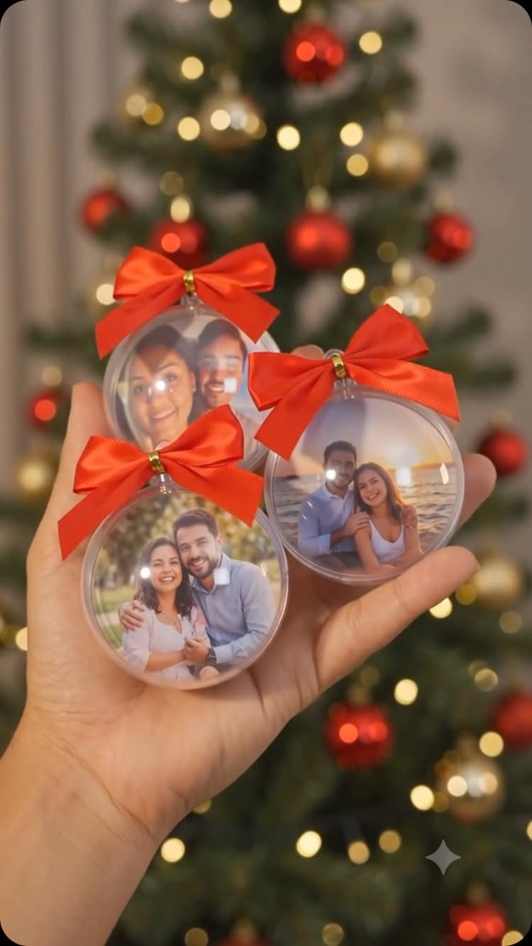 Three clear spherical Christmas ornaments with photos and red bows held in a hand.