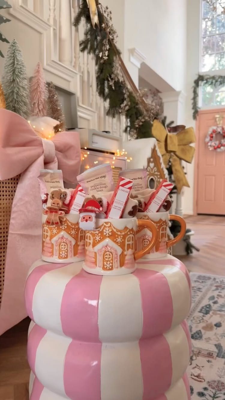 Gingerbread house mugs filled with treats on a pink striped pedestal.