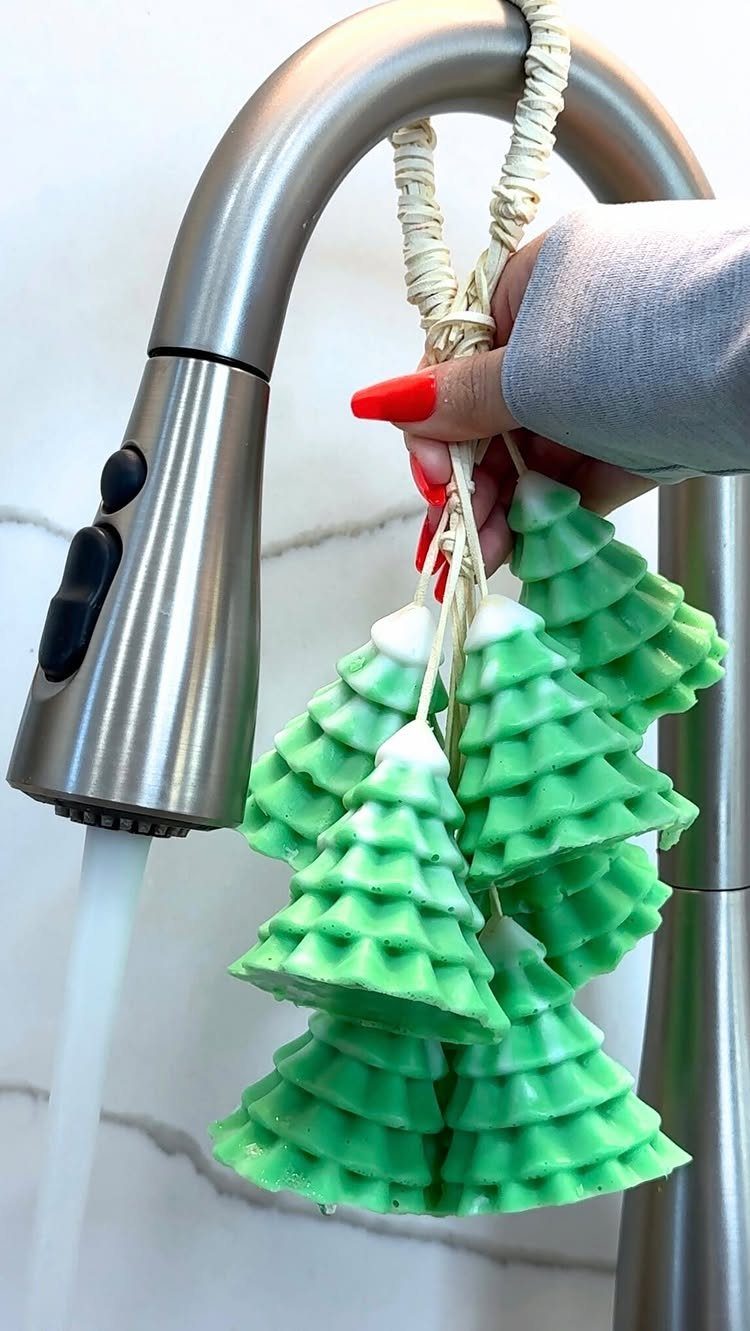 Green Christmas tree shaped soaps hanging from a silver kitchen faucet.