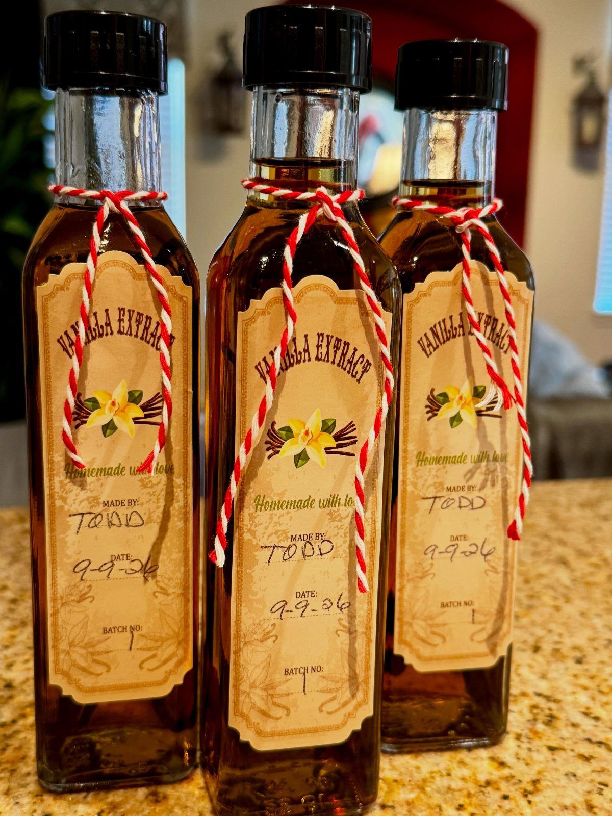 Three bottles of homemade vanilla extract with labels and red striped twine ribbons.