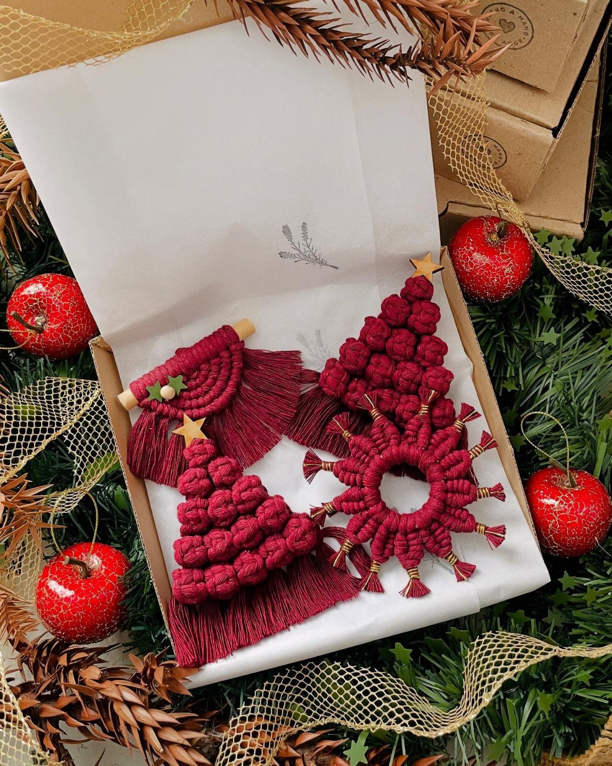 Red macrame Christmas tree and star ornaments in a gift box with pine needles.