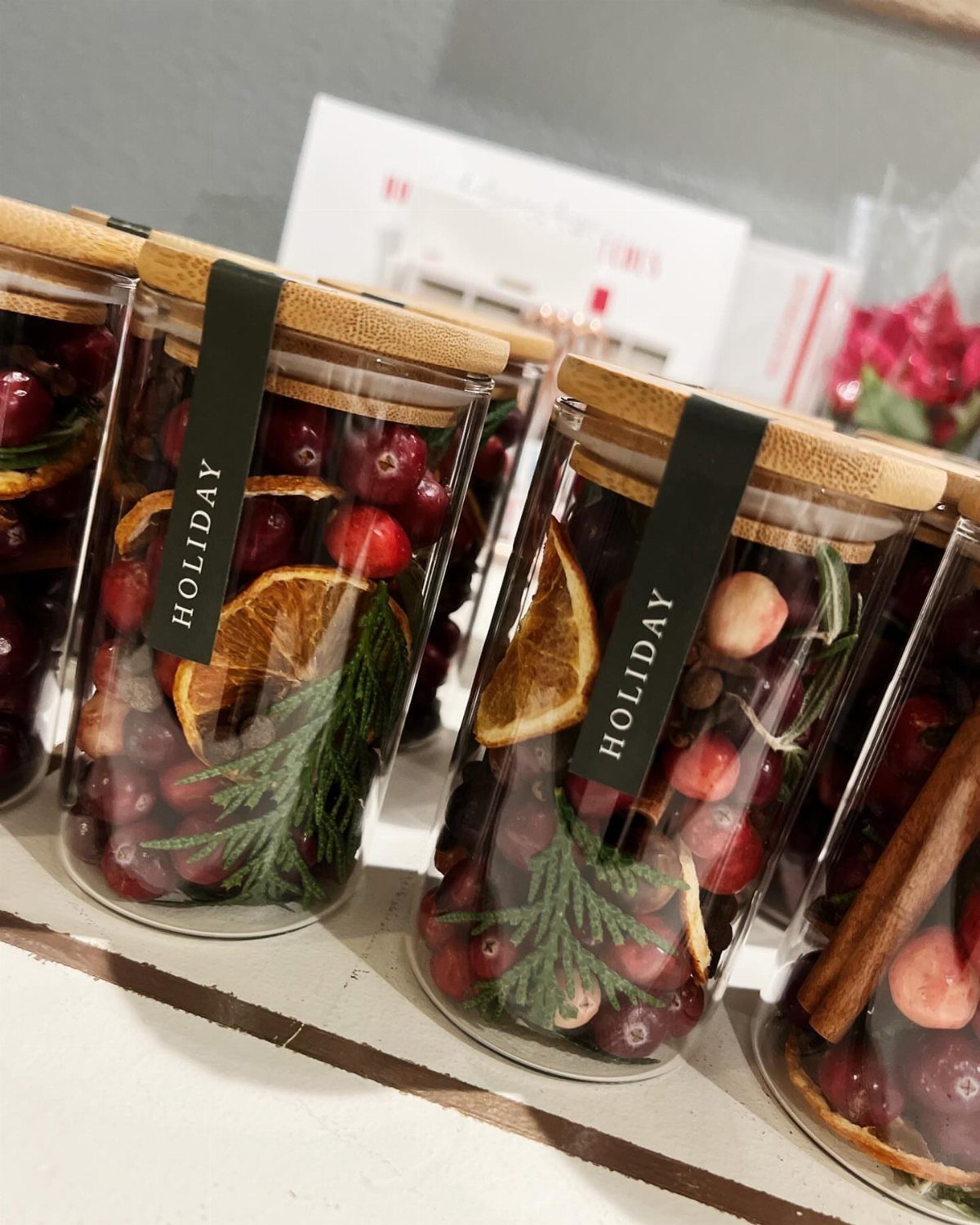 Glass jars filled with cranberries, dried orange slices, and pine needles for holiday spices.
