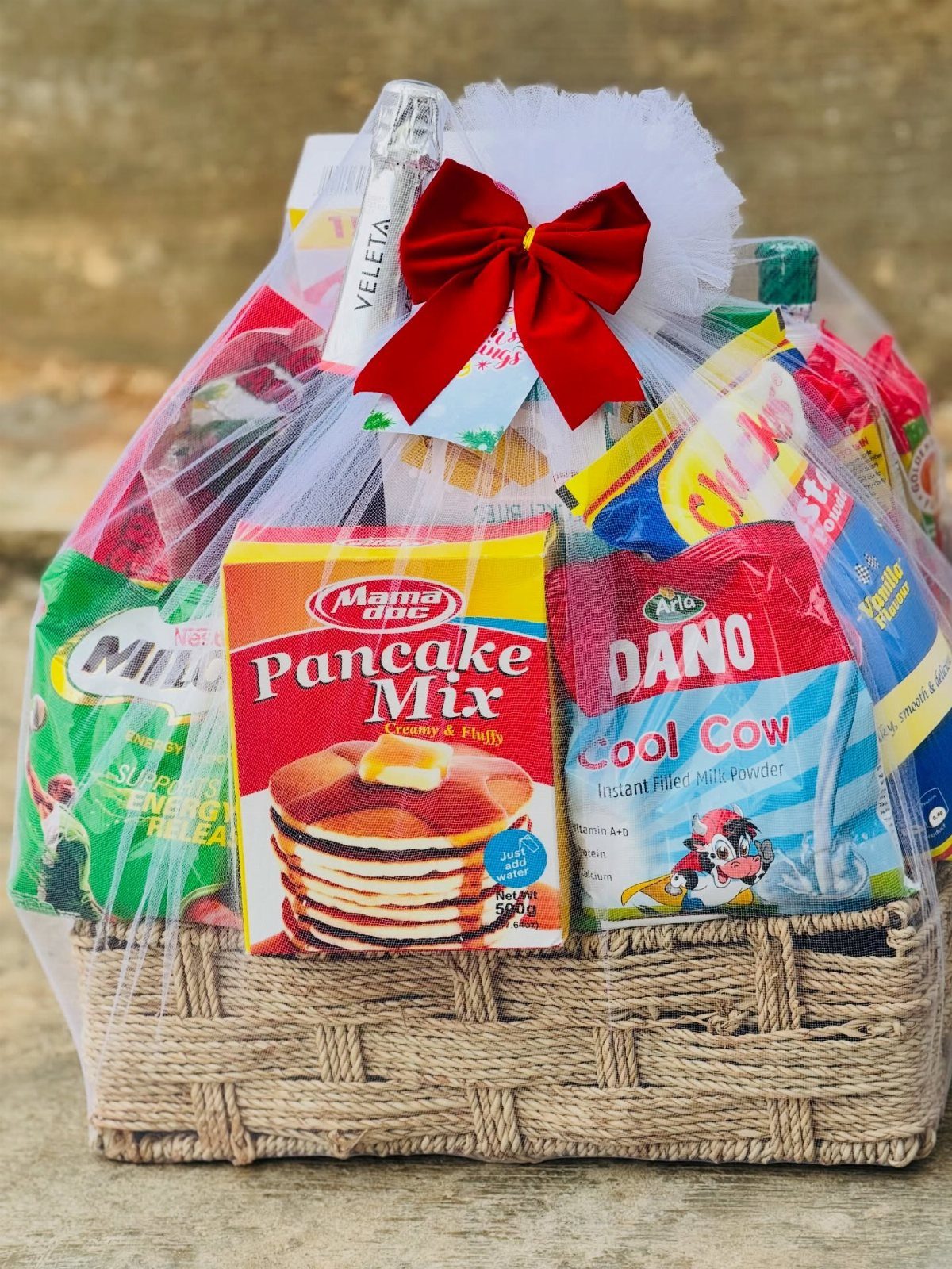Wicker gift basket containing pancake mix and other breakfast items wrapped in cellophane.