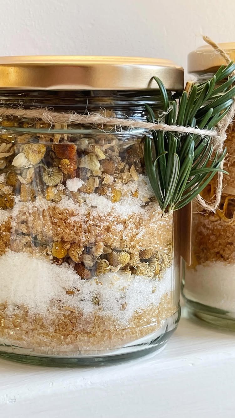 Glass jars filled with layered sugar scrub and dried herbs tied with rosemary.