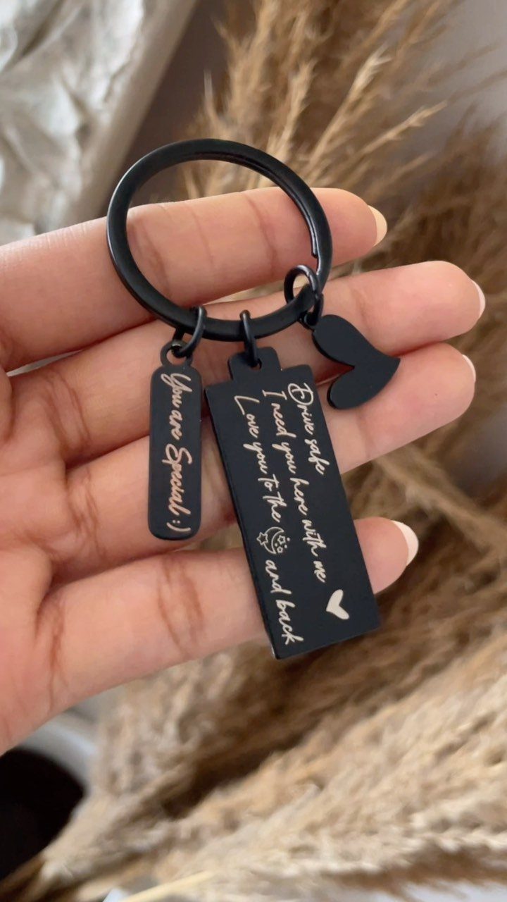 Black metal personalized keychain with engraved romantic messages held in a hand.