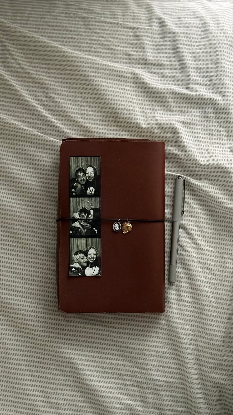 Brown leather journal with black and white photos and a silver pen on striped fabric