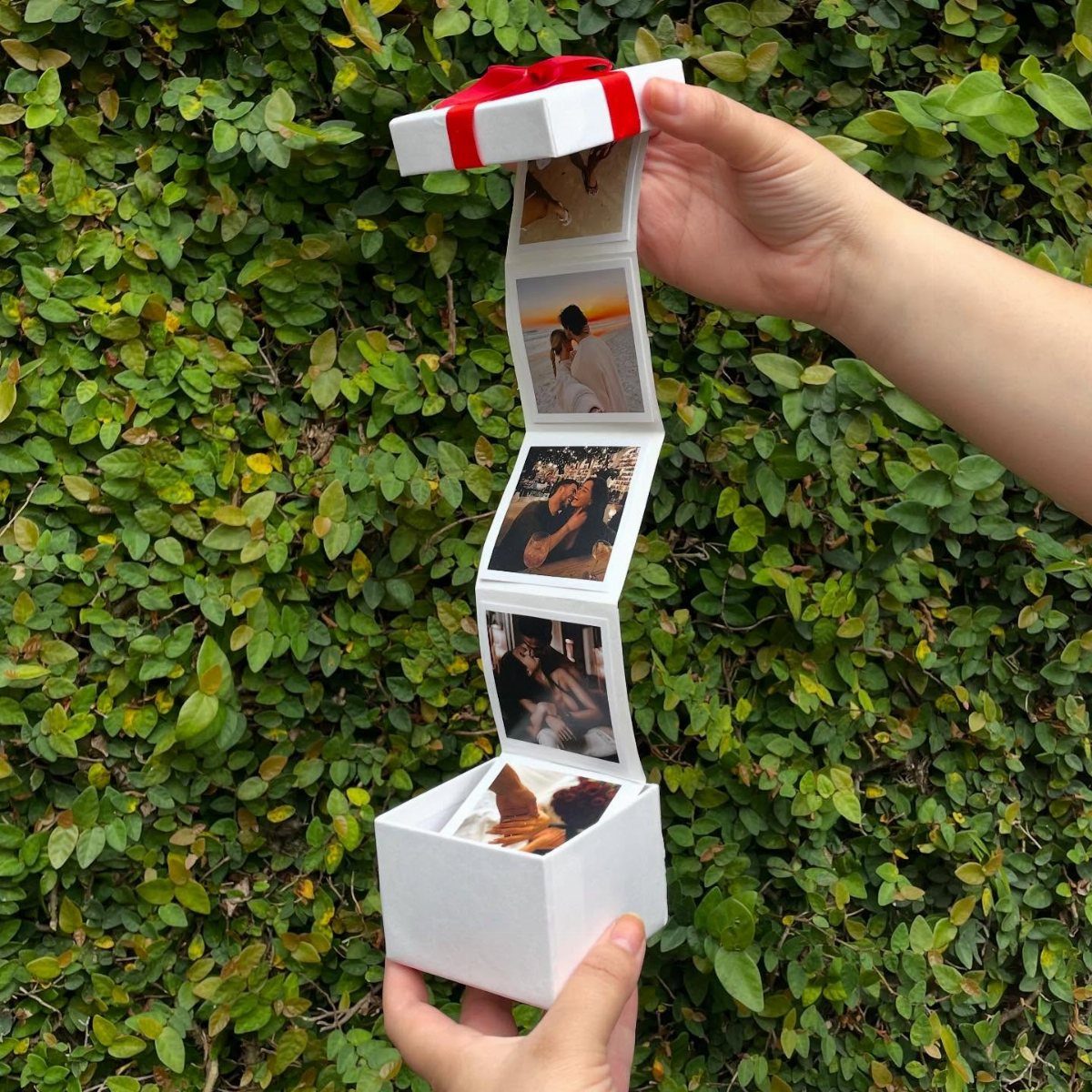 White cube gift box opening to reveal a folding strip of couple photos