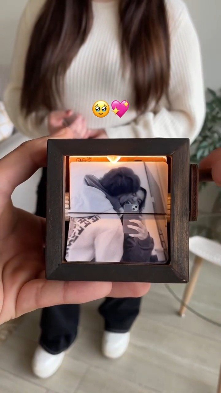 Hand holding a small wooden light box with a glowing couple's photo inside
