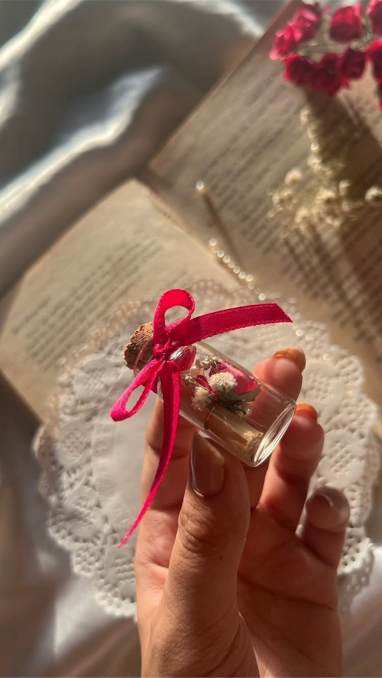 Small glass vial with dried flowers and a scroll tied with pink ribbon