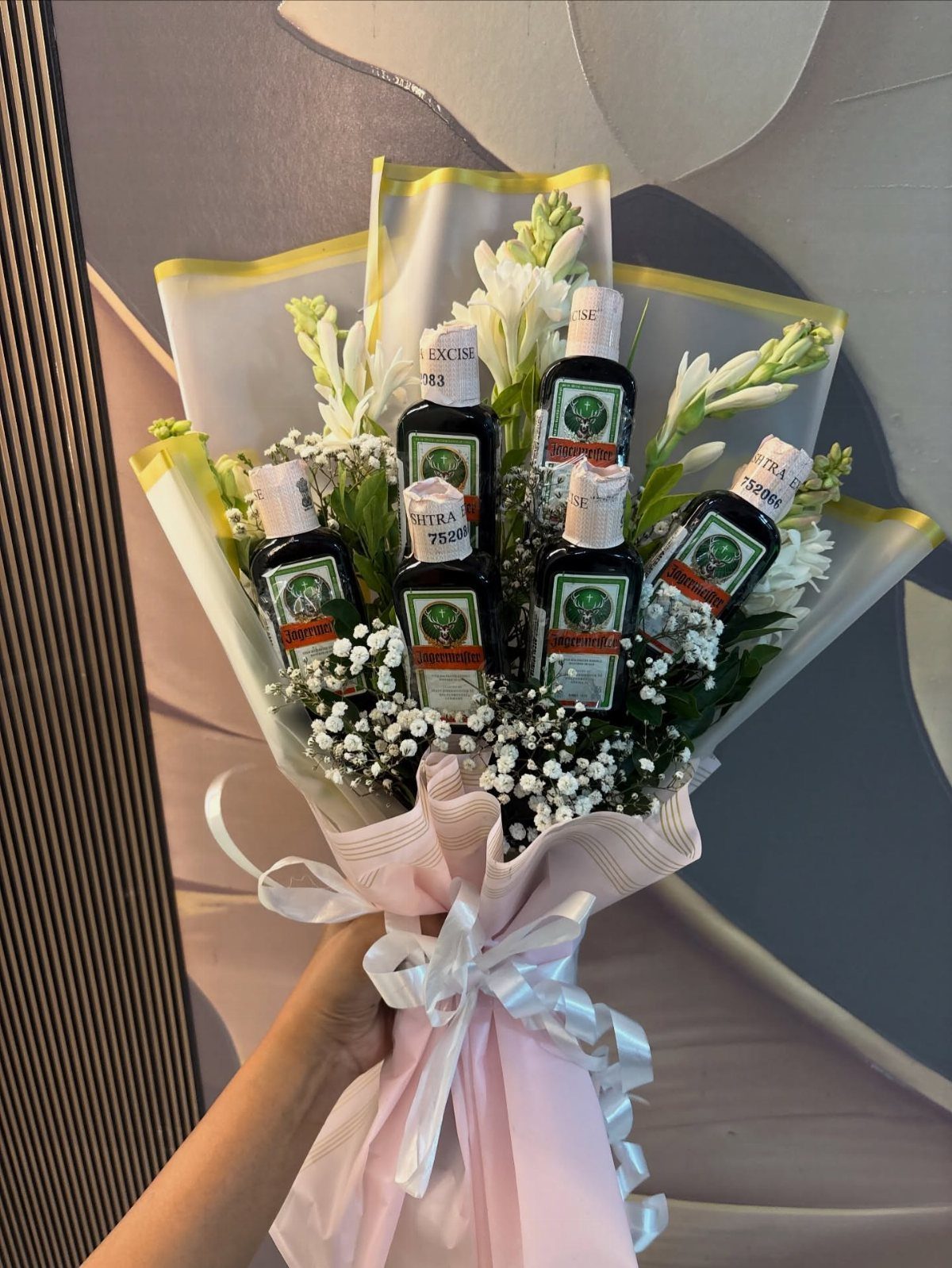 Bouquet of white flowers and small liquor bottles wrapped in pink paper