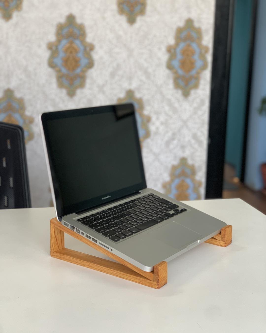 Silver laptop resting on a light wooden riser stand on a white table