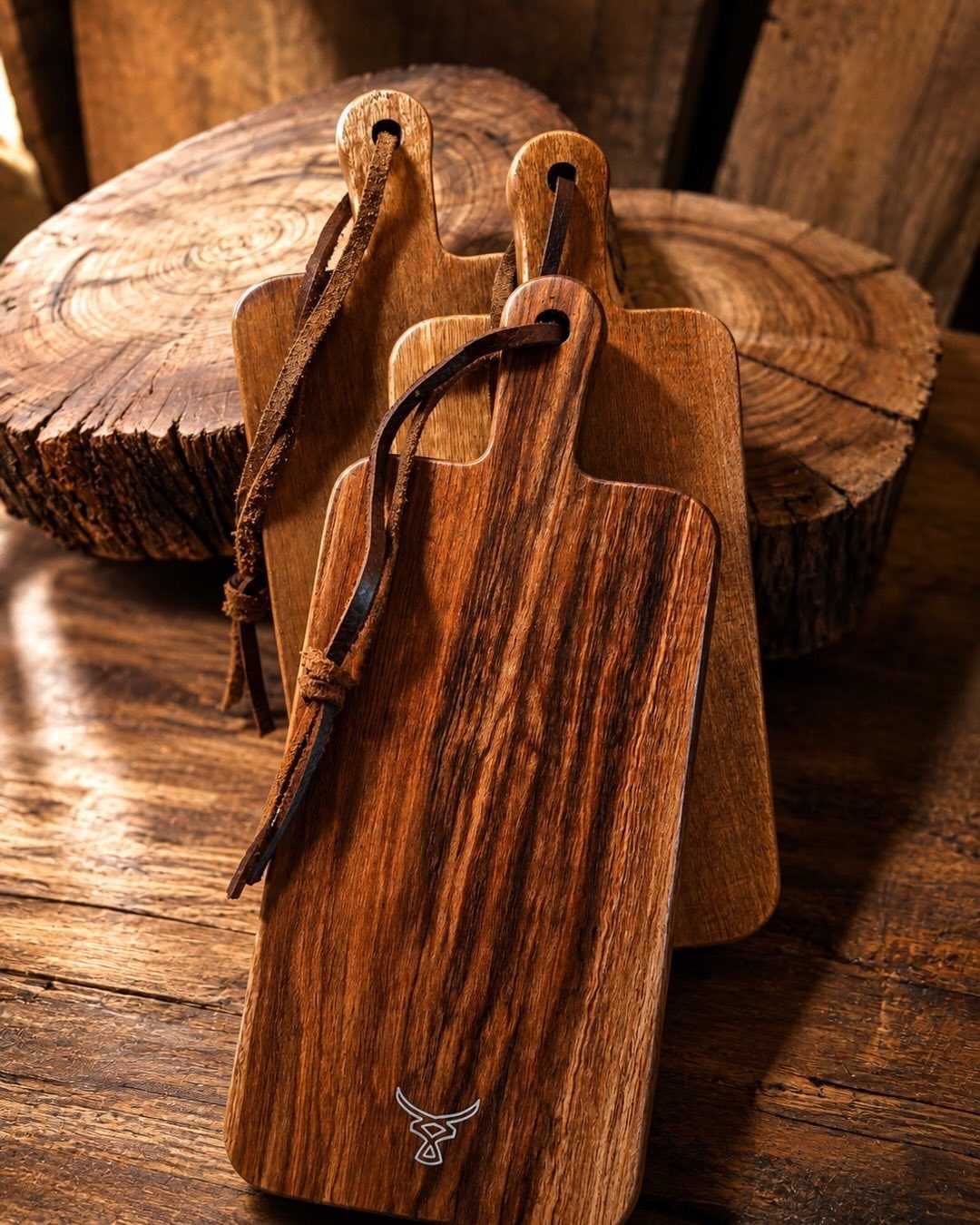 Wooden cutting boards with leather strap handles resting on a rustic wooden table