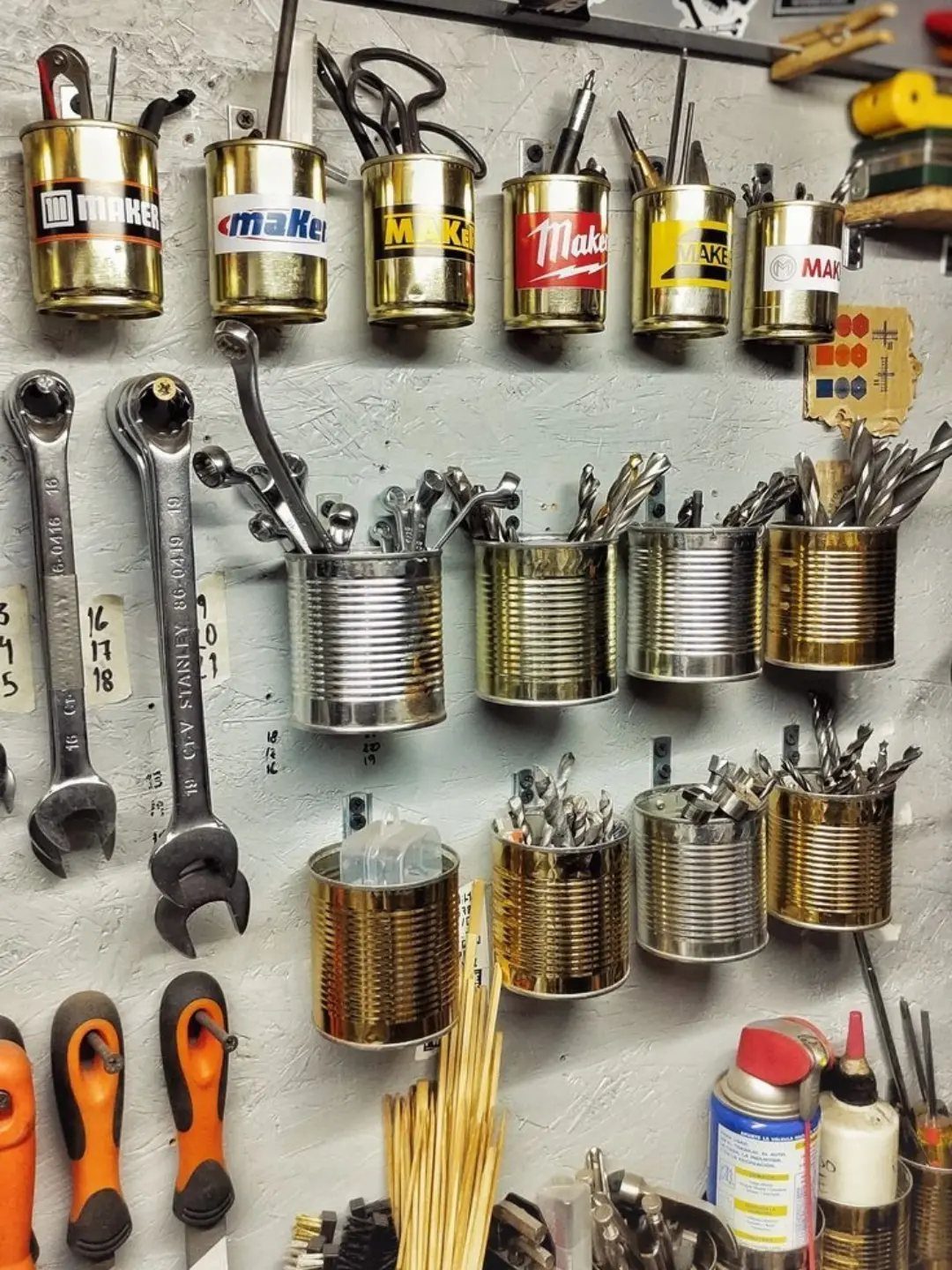 Metal cans mounted on a wall holding various hand tools and drill bits.
