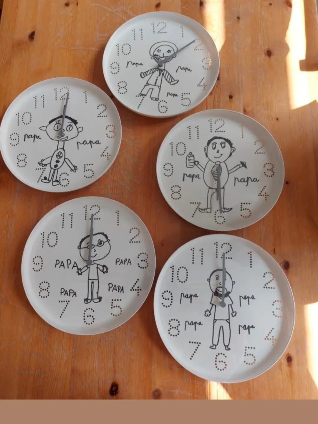Five white DIY wall clocks with child-like drawings of a father on wood.