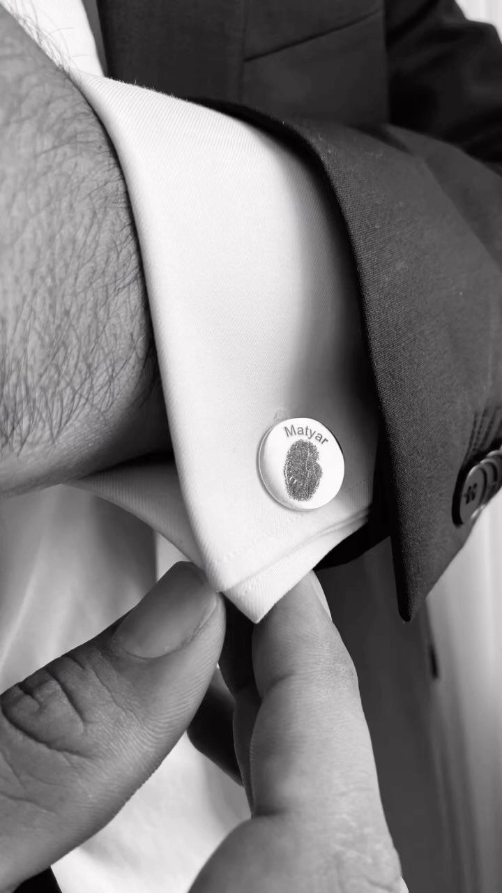Silver cufflink with a fingerprint and name on a white dress shirt sleeve.