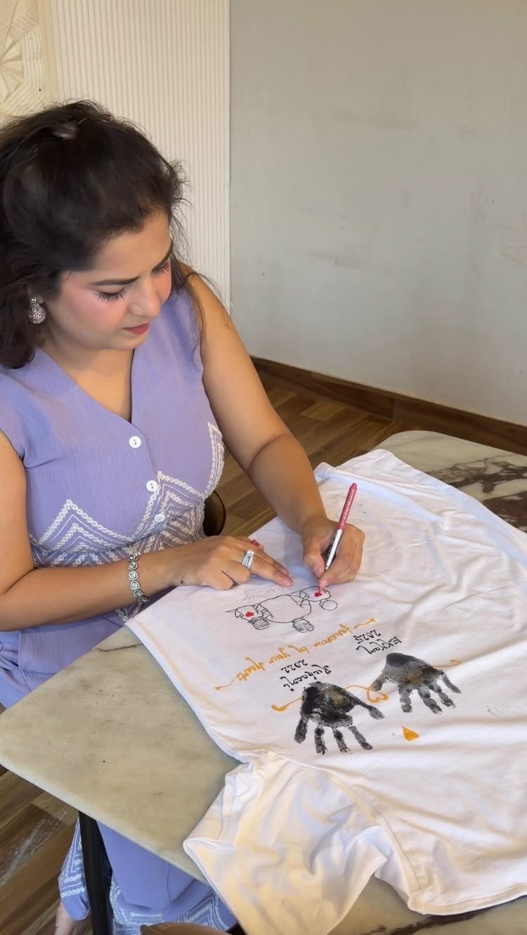 Woman drawing a car and adding handprints to a white t-shirt as a gift.