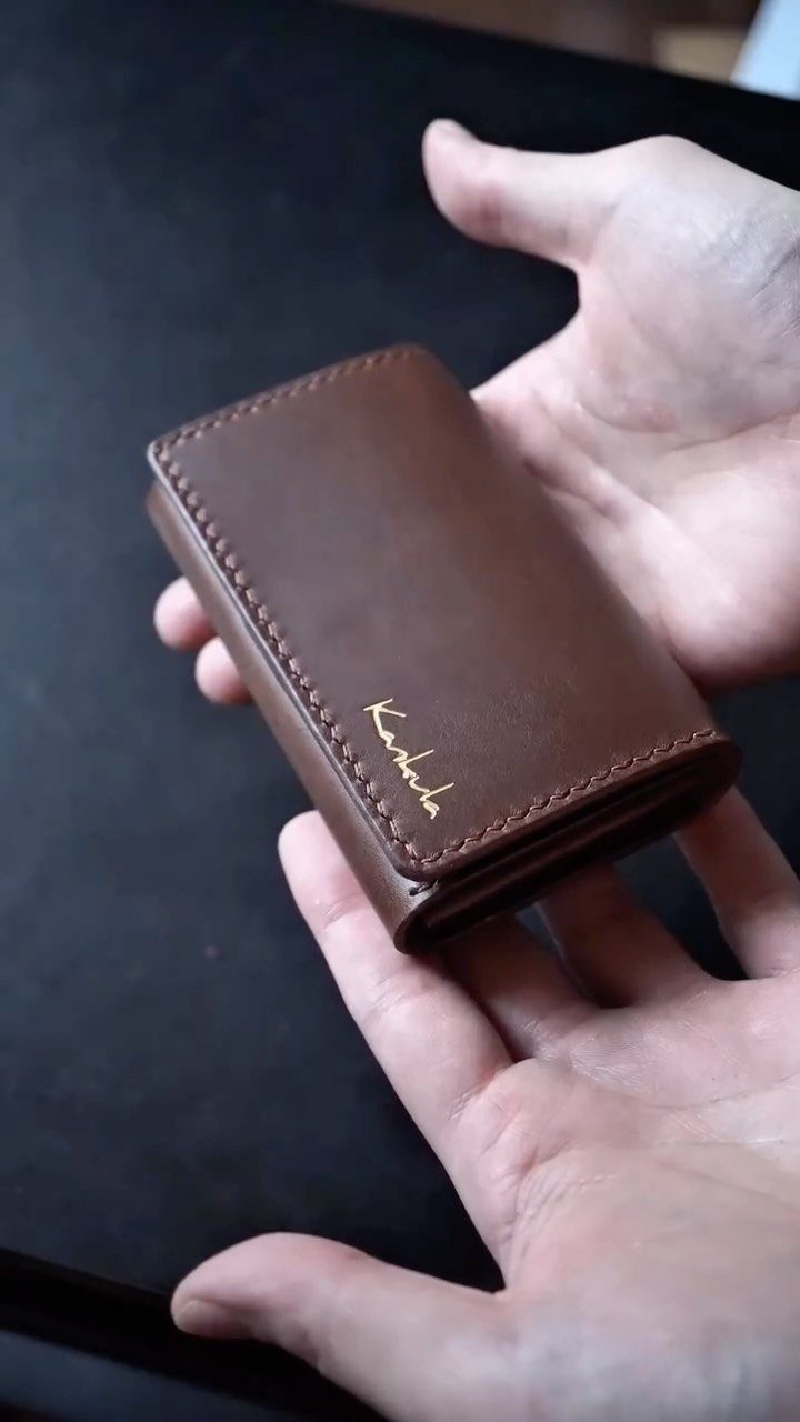 Brown leather wallet with gold engraving held in two open hands.