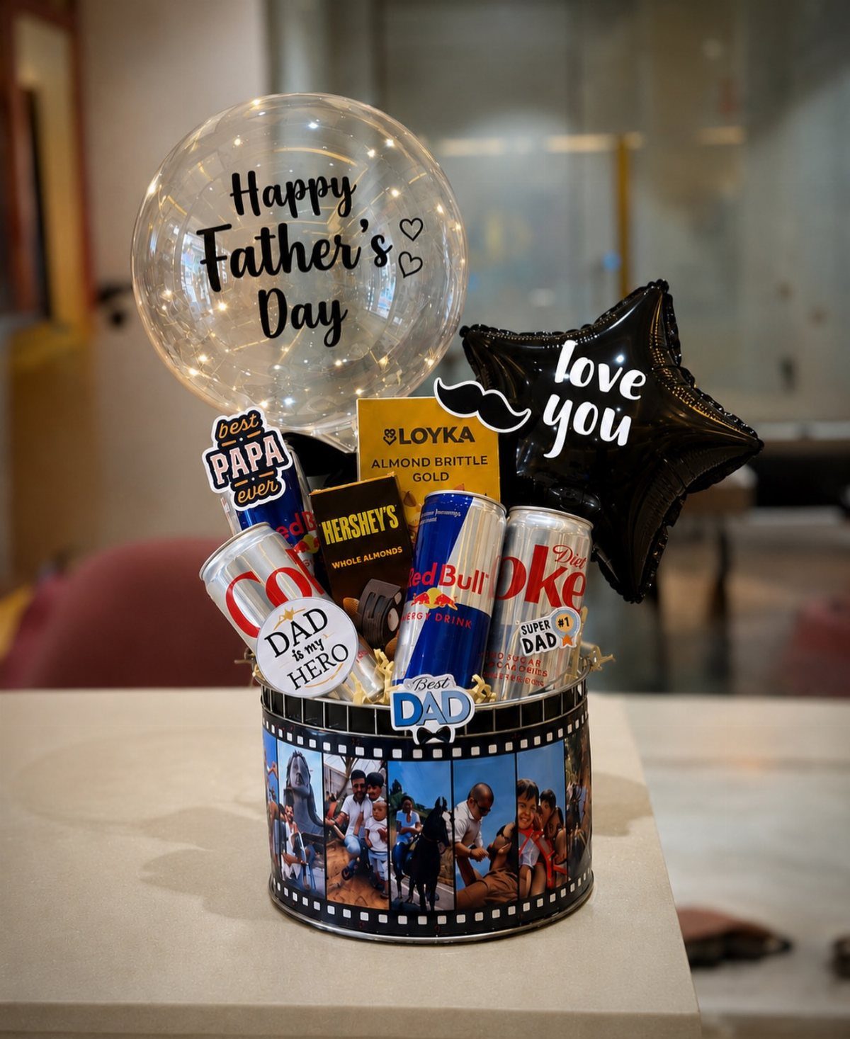 Father's Day gift basket with drinks, snacks, and balloons in a photo-decorated container.