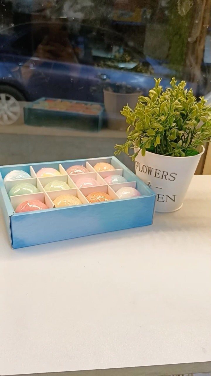 Colorful round bath bombs in a blue divided gift box next to a plant