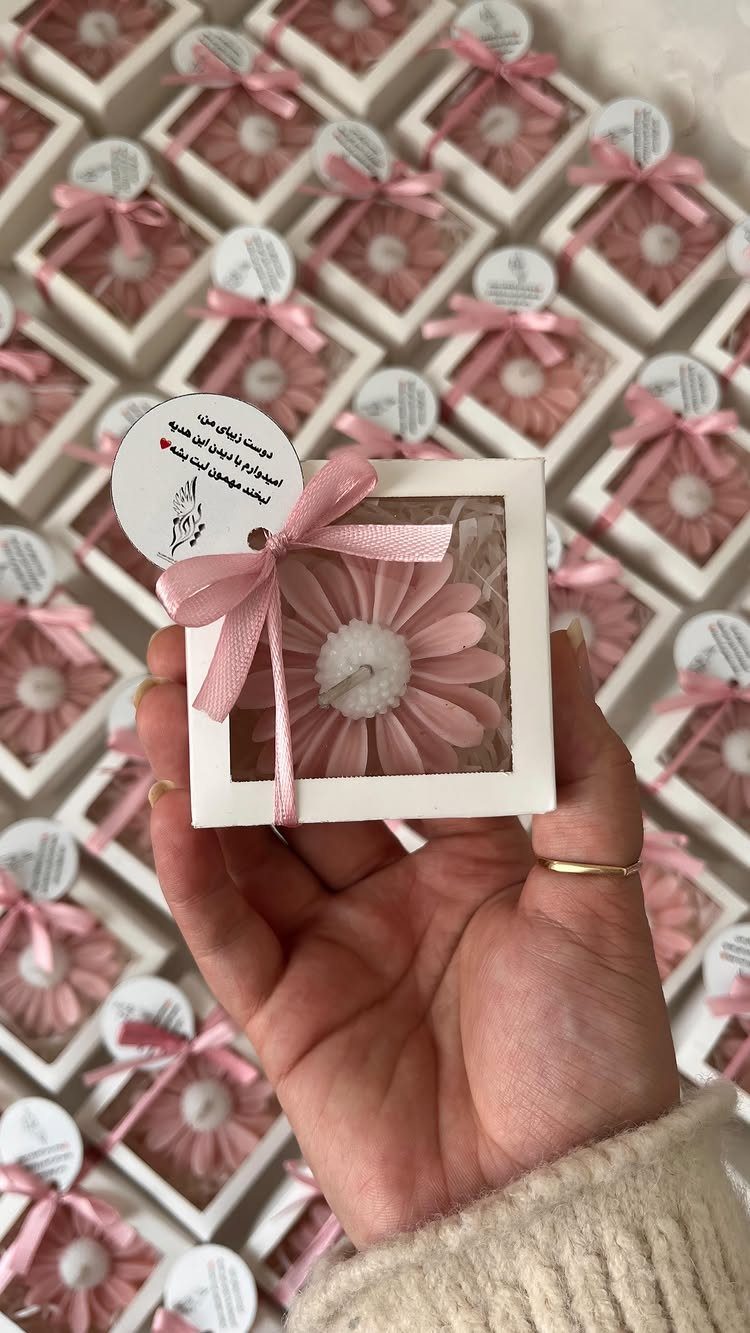 Pink flower-shaped candles in small white gift boxes with pink ribbons and tags.