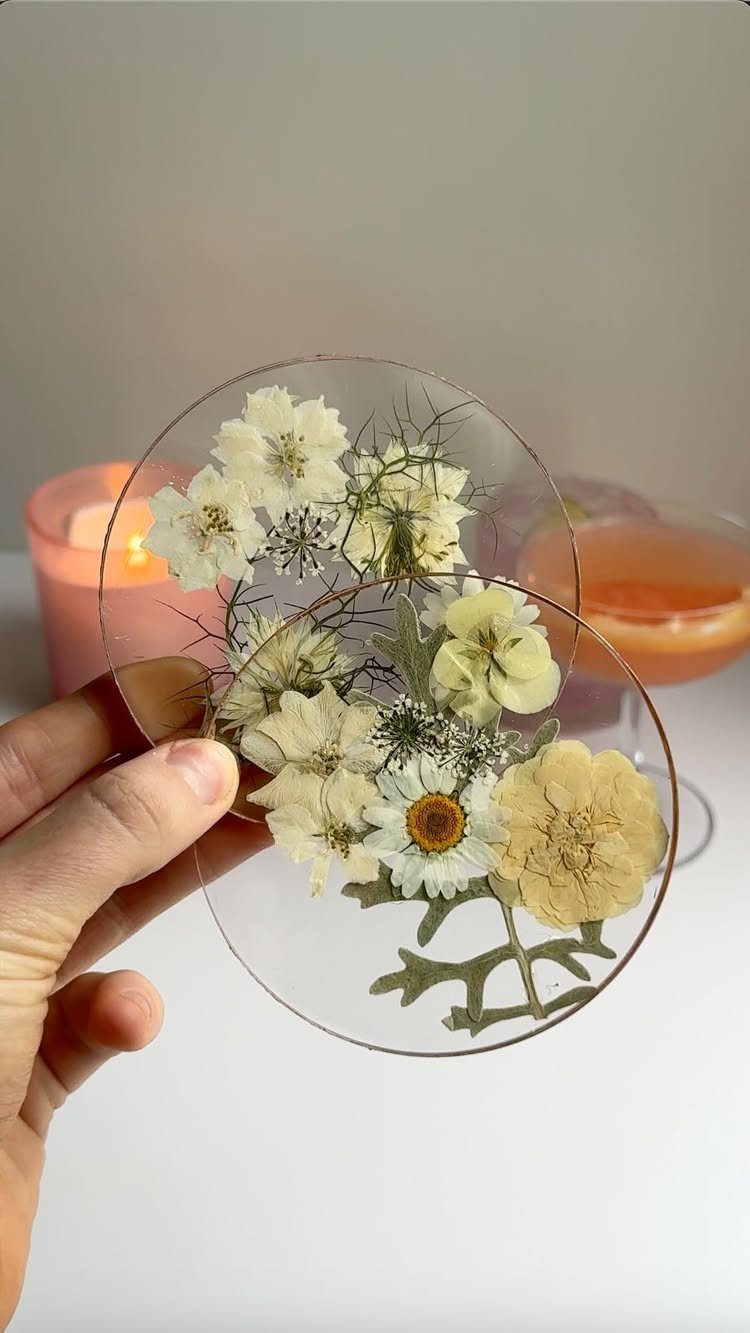 Two circular transparent resin coasters with pressed white and yellow flowers inside.