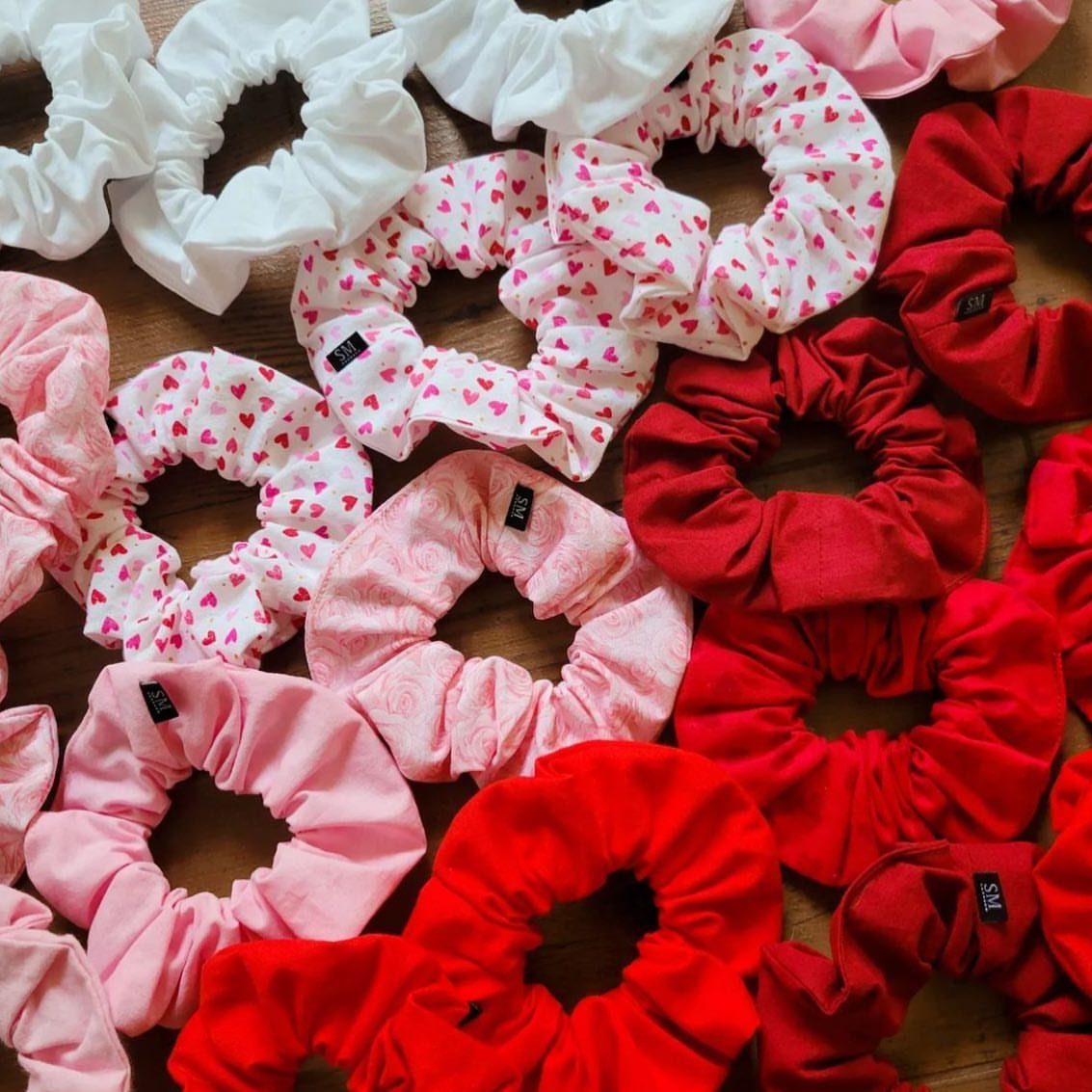Fabric hair scrunchies in red, pink, and white scattered on a wooden surface.