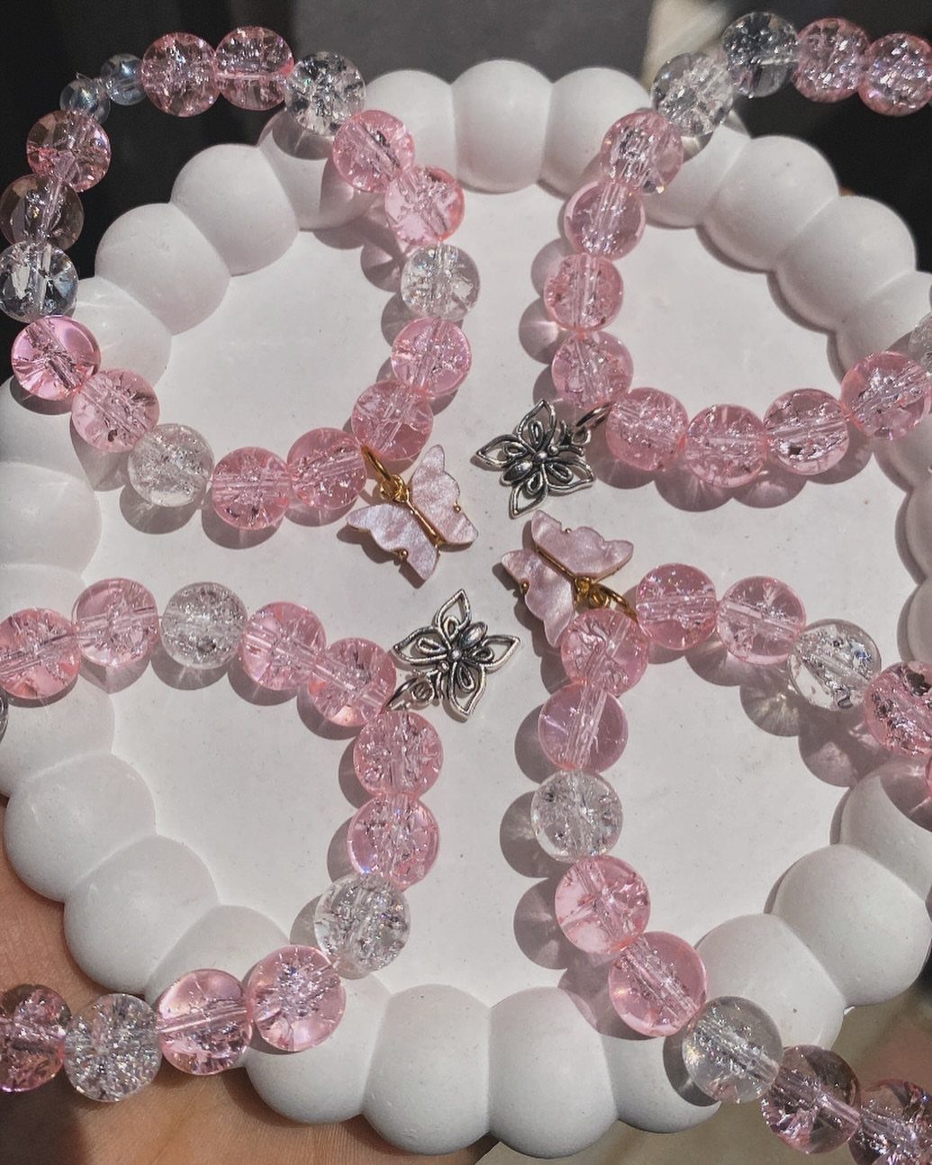 Pink and clear beaded bracelets with butterfly charms on a white beaded tray