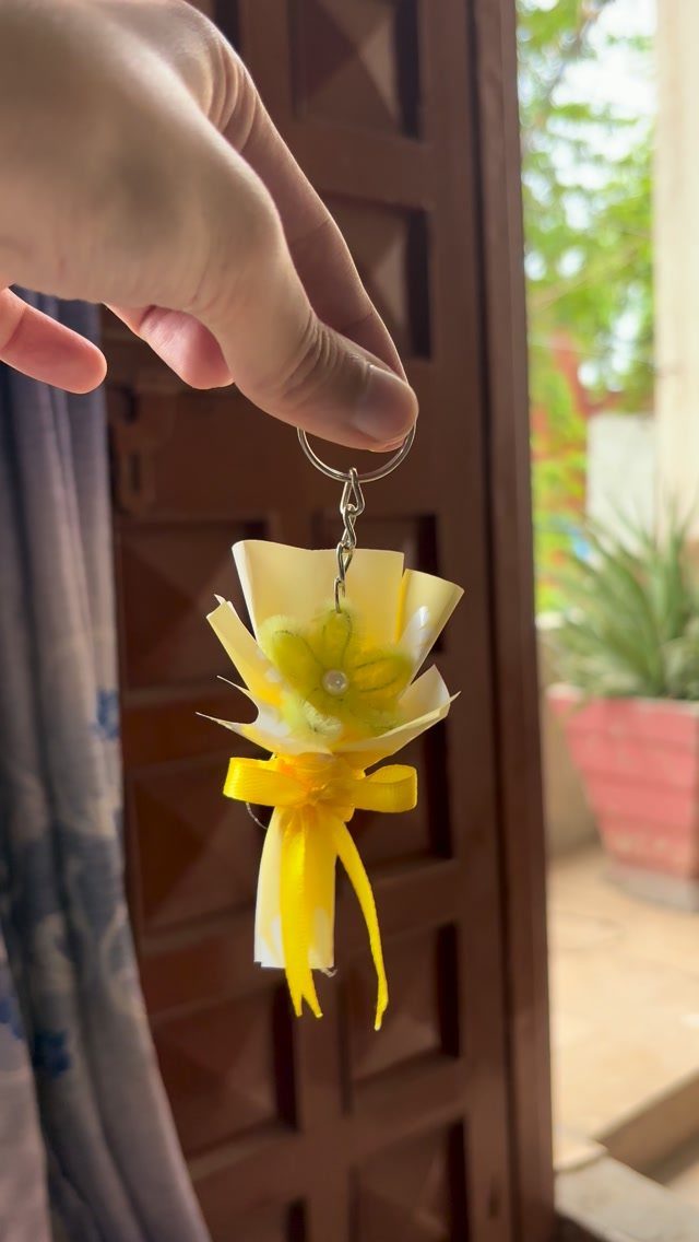 Hand holding a miniature yellow flower bouquet keychain with a yellow ribbon.