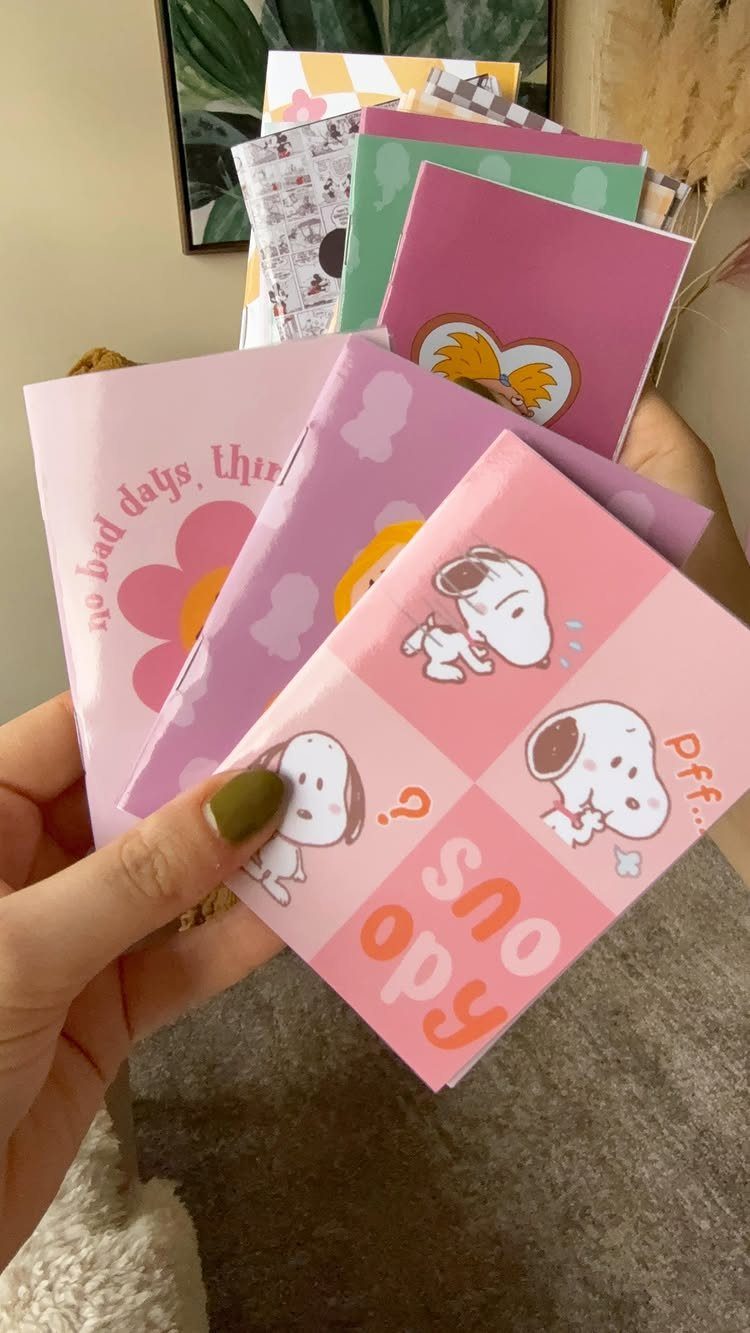 Colorful small notebooks with Snoopy and floral designs held in a person's hand.