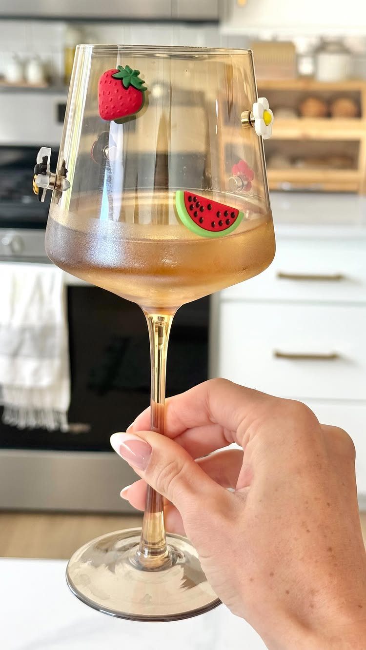 Hand holding a decorated wine glass with fruit and flower charms attached.