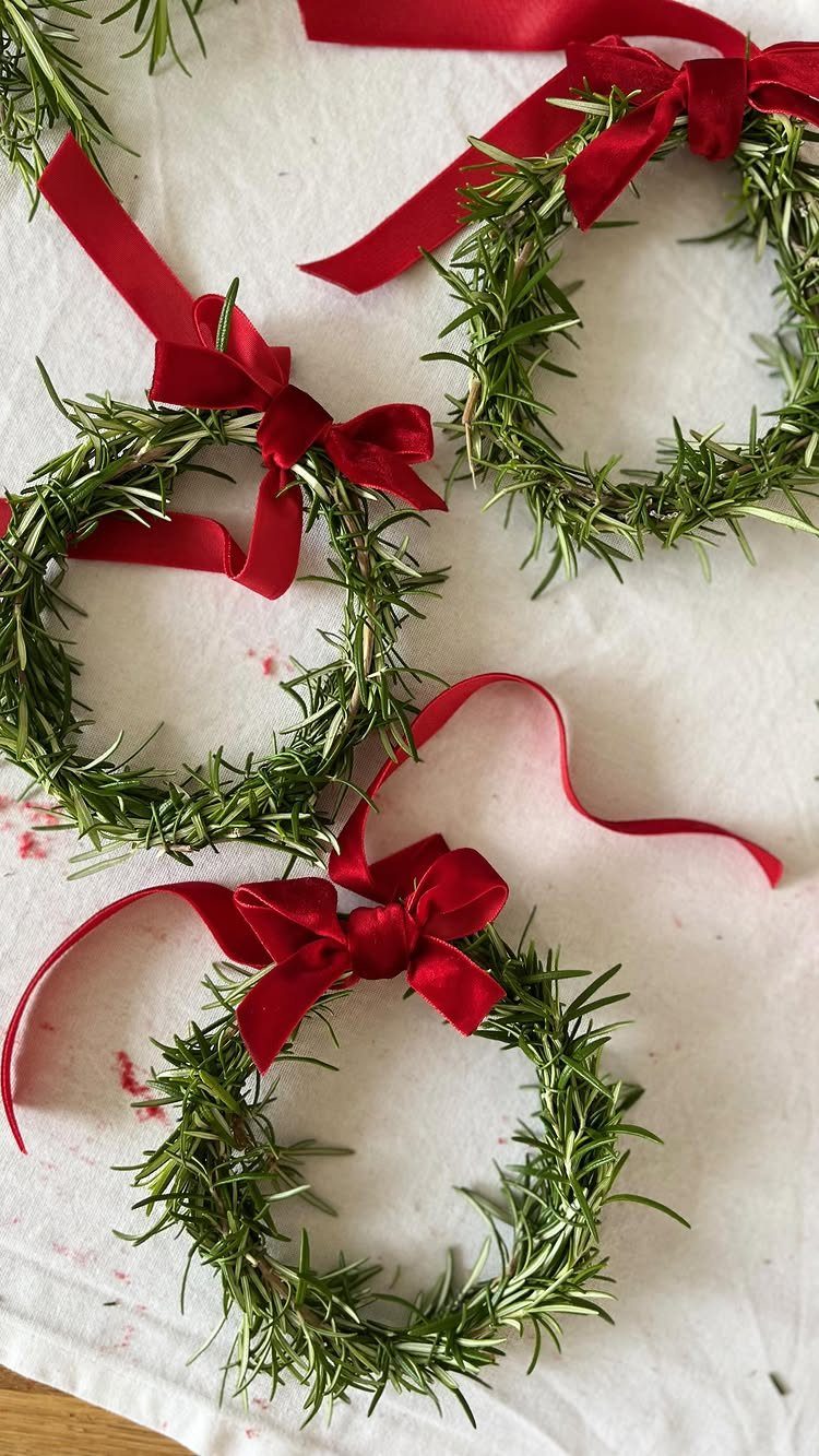 Three small rosemary wreaths with red satin bows on a white cloth background.