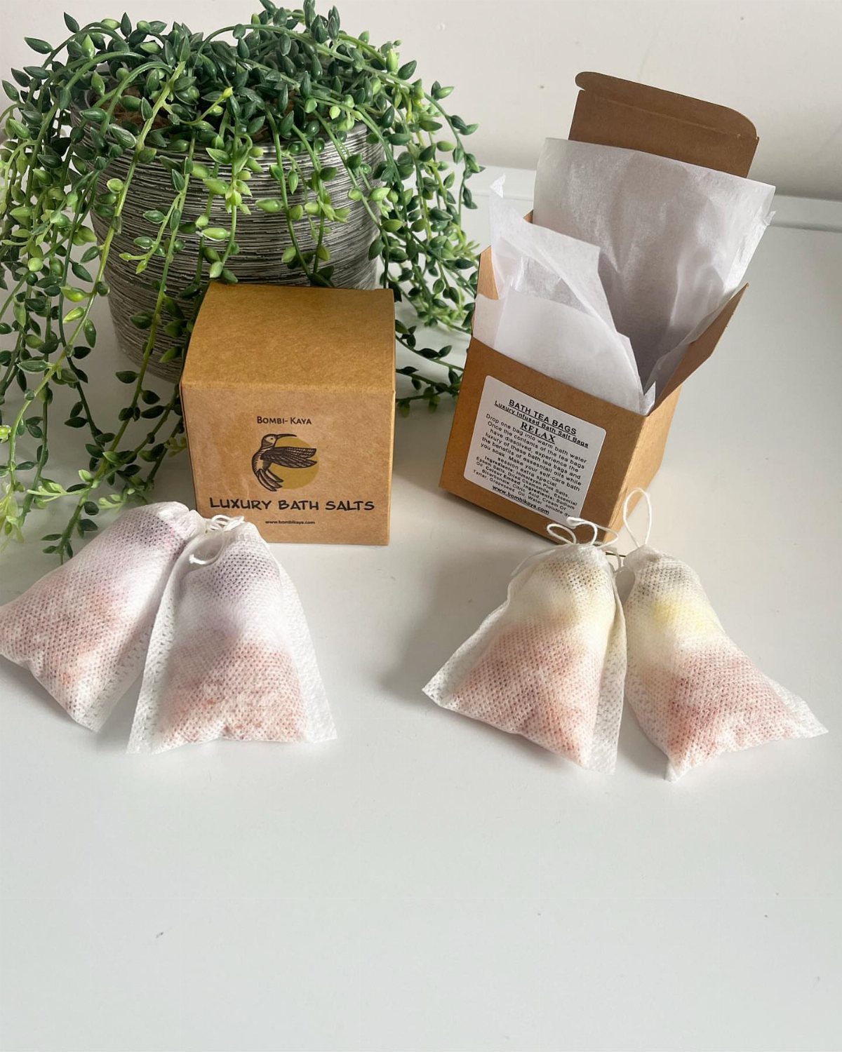 White fabric bath tea bags and brown gift boxes next to a green plant