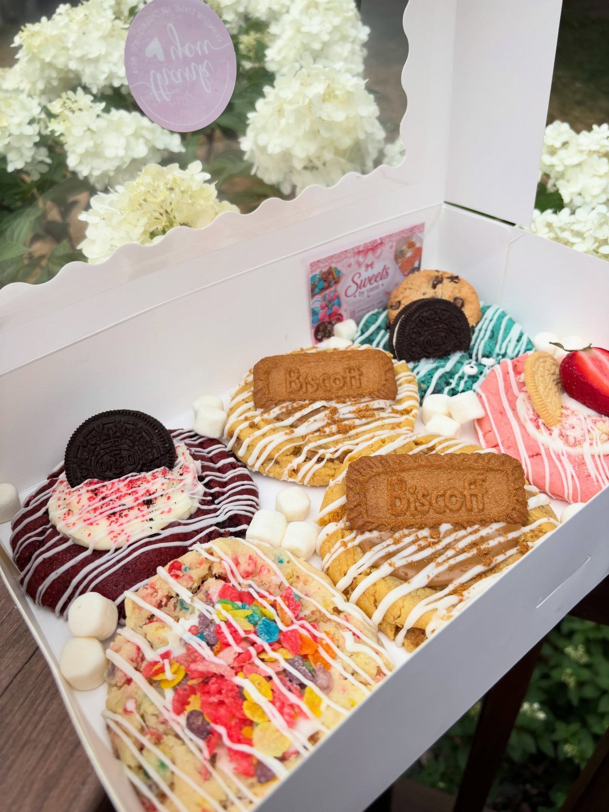 Decorated gourmet cookies with various toppings in a white gift box.