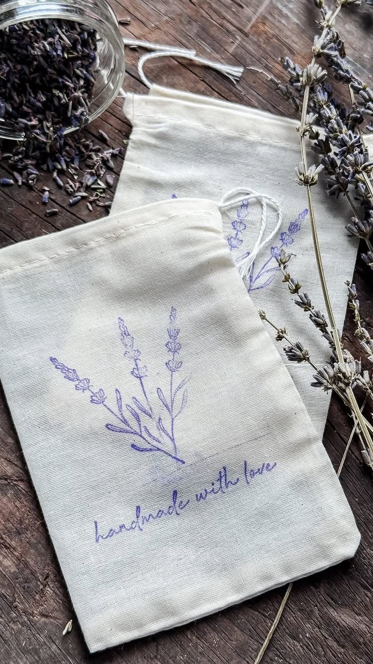 Two fabric drawstring sachets with lavender illustrations and dried lavender on wood.