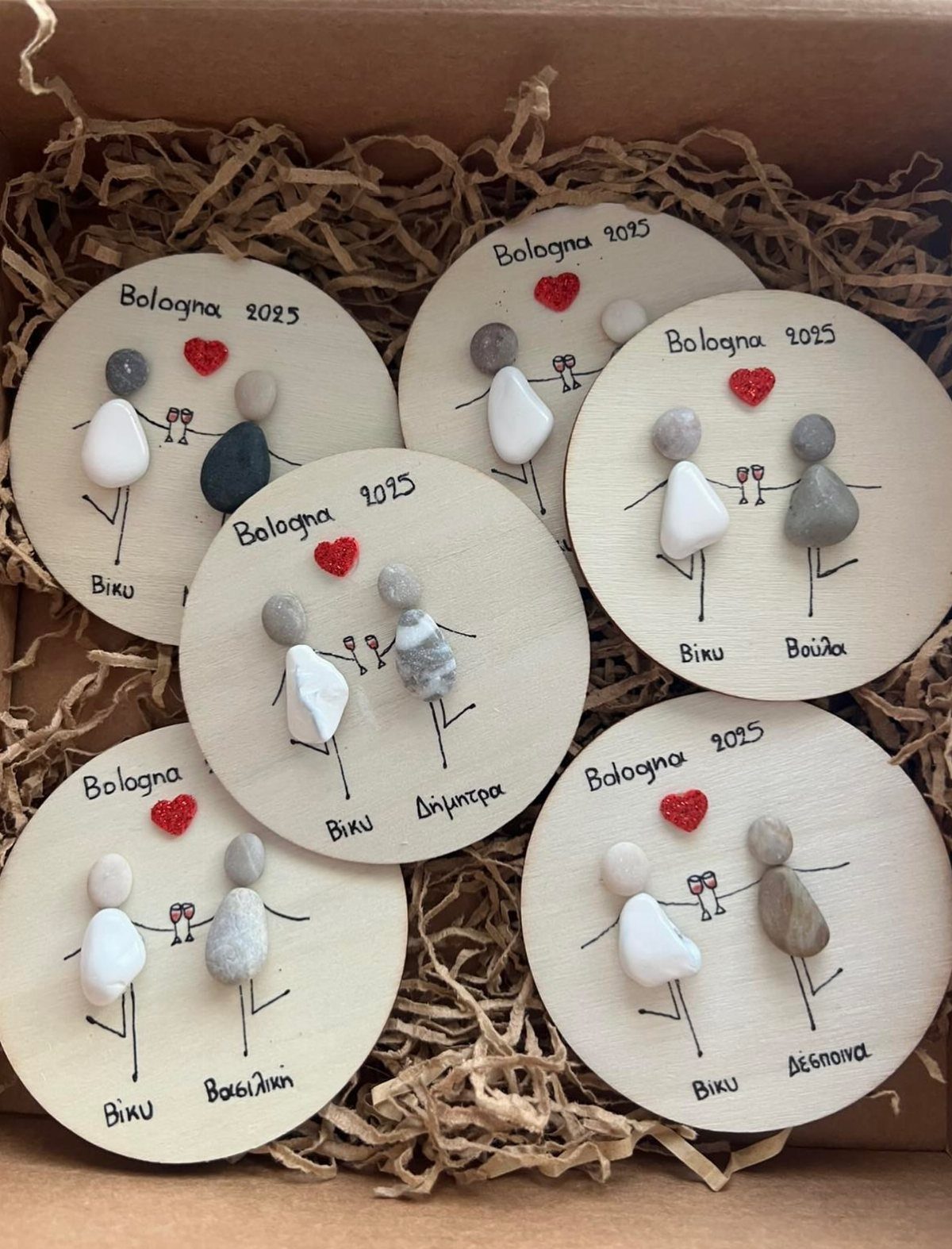 Circular wooden discs with pebble art figures and handwritten text in a box