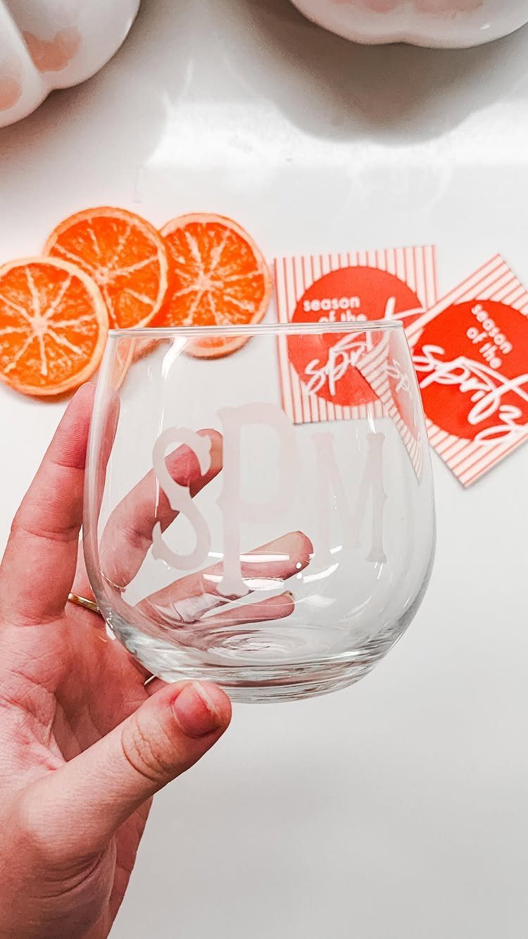Etched glass with initials held by a hand near dried orange slices