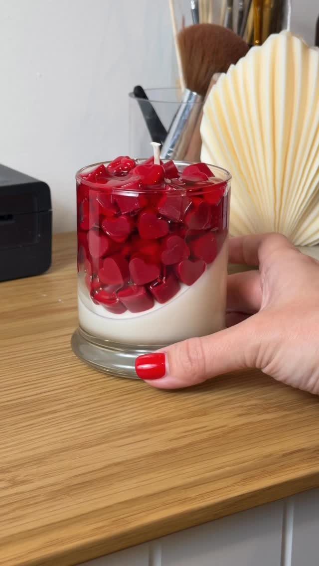 Hand holding a glass jar candle filled with red heart-shaped wax pieces.