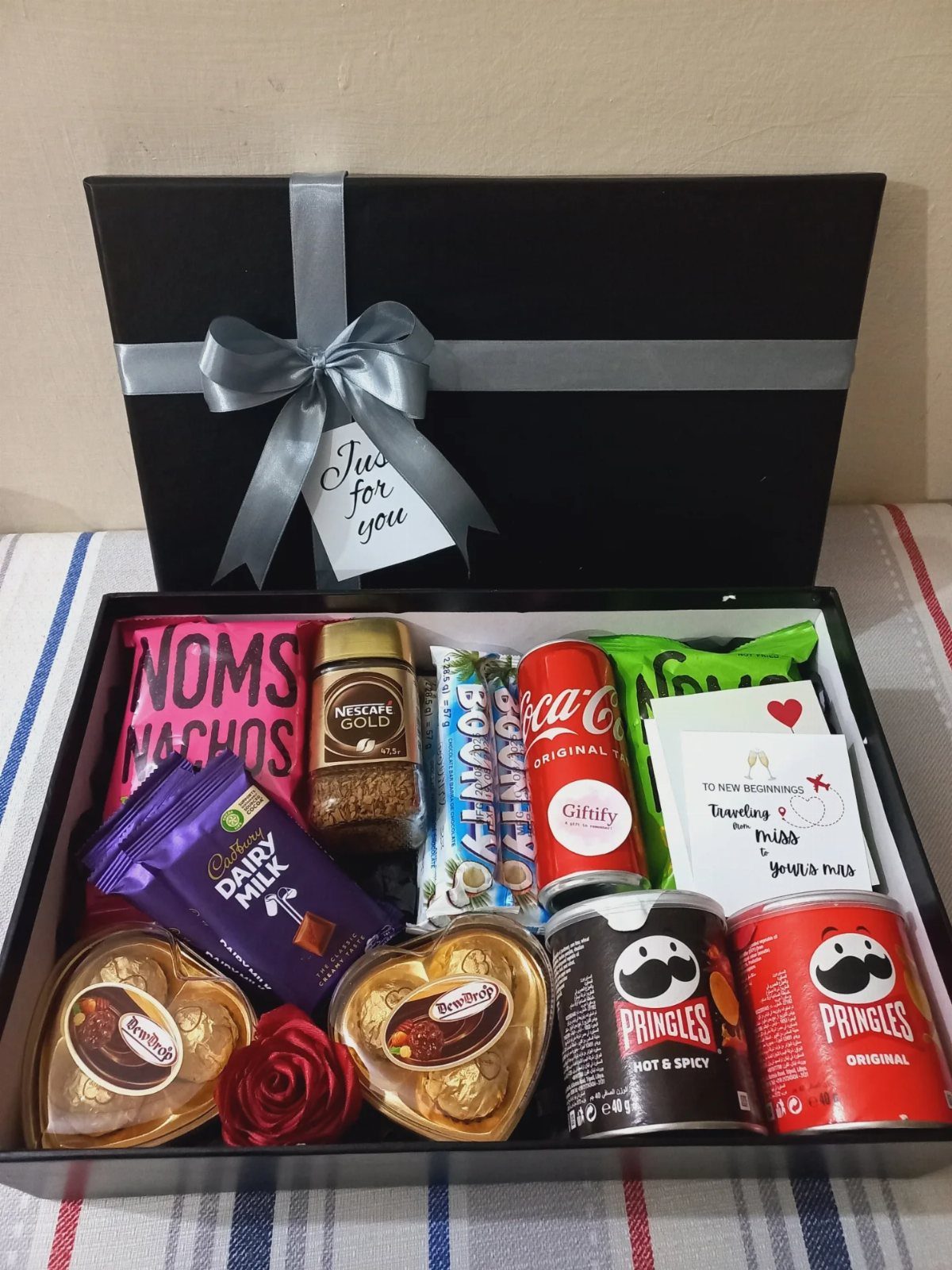 Black gift box filled with assorted chocolates, chips, and drinks for Valentine's Day.