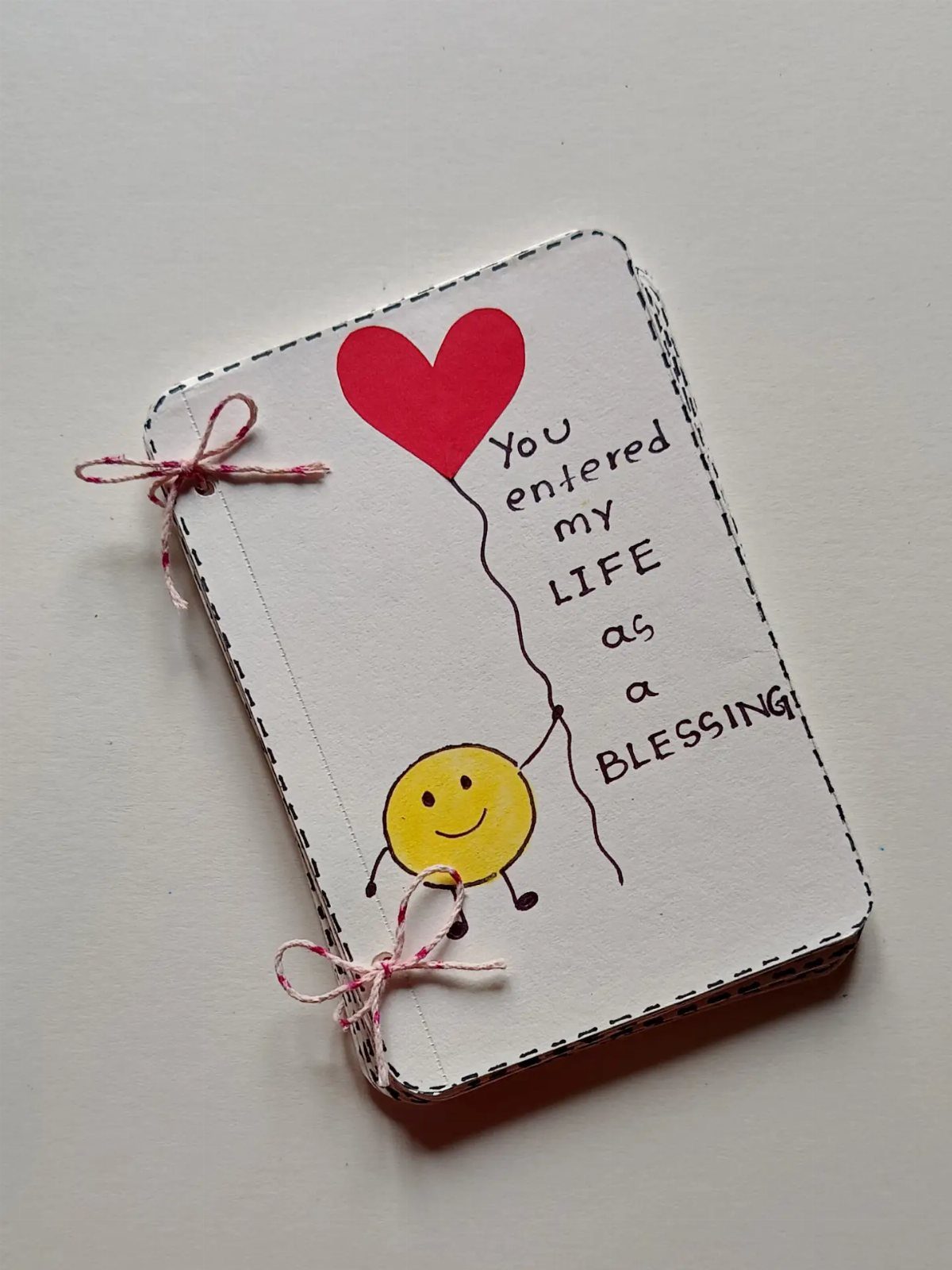 Handmade white notebook with a smiley face holding a red heart balloon.
