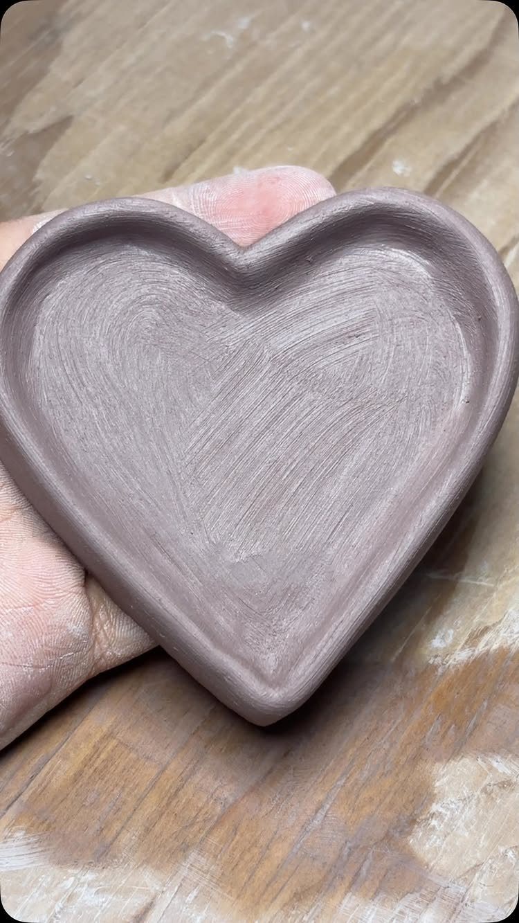 Heart-shaped clay dish held in a hand over a wooden surface