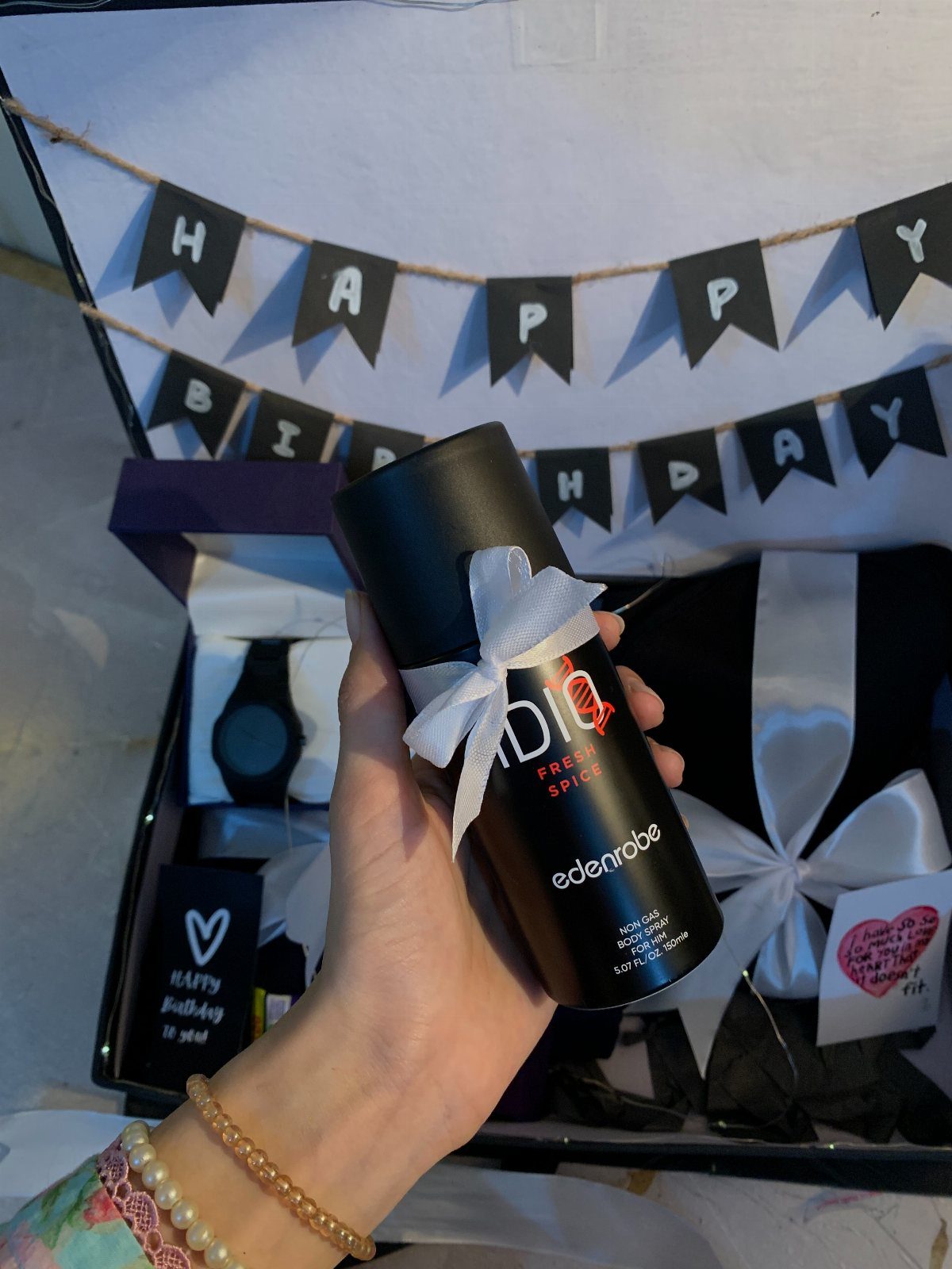 Hand holding a gift tube over a curated birthday gift box for men.