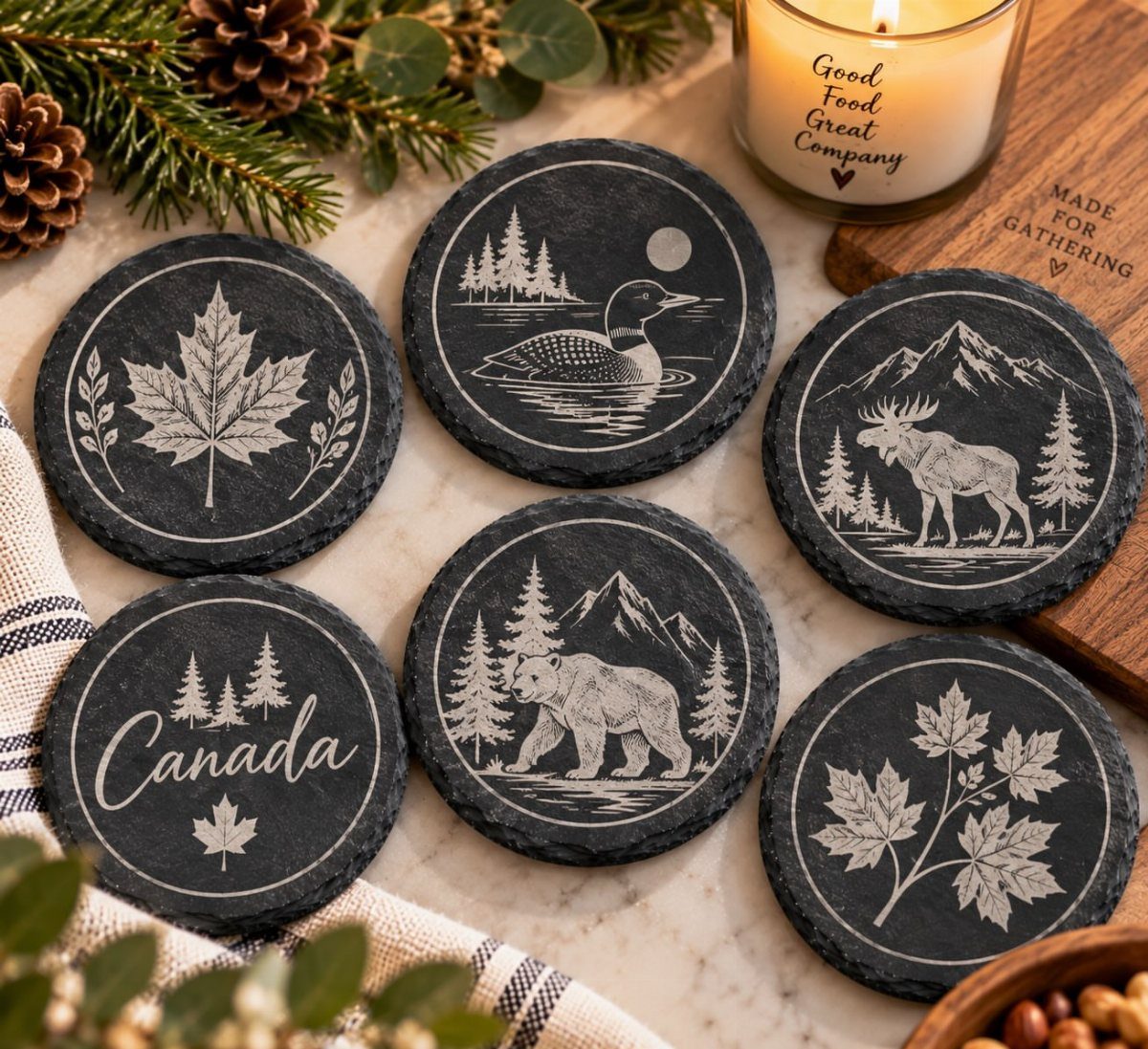 Six black slate coasters with white nature engravings on a marble surface.