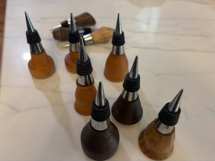Handcrafted wooden bottle stoppers with metal tips arranged on a white marble surface.